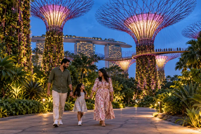 Indian family walking beneath illuminated Singapore Supertrees at dusk