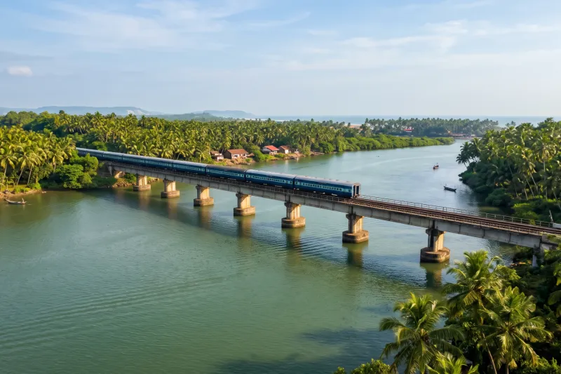 Konkan Railway train crossing a river bridge between coconut palms in Goa
