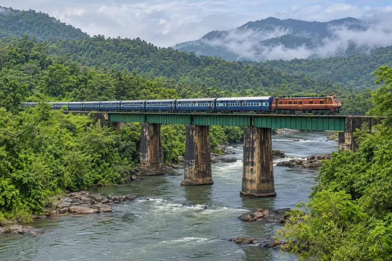 Passenger train crossing a river bridge in the Western Ghats