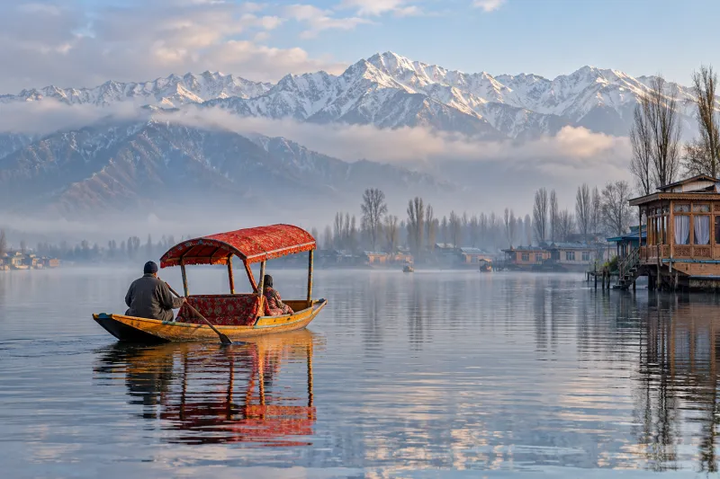 Red shikara crossing misty Dal Lake beneath snowy mountains